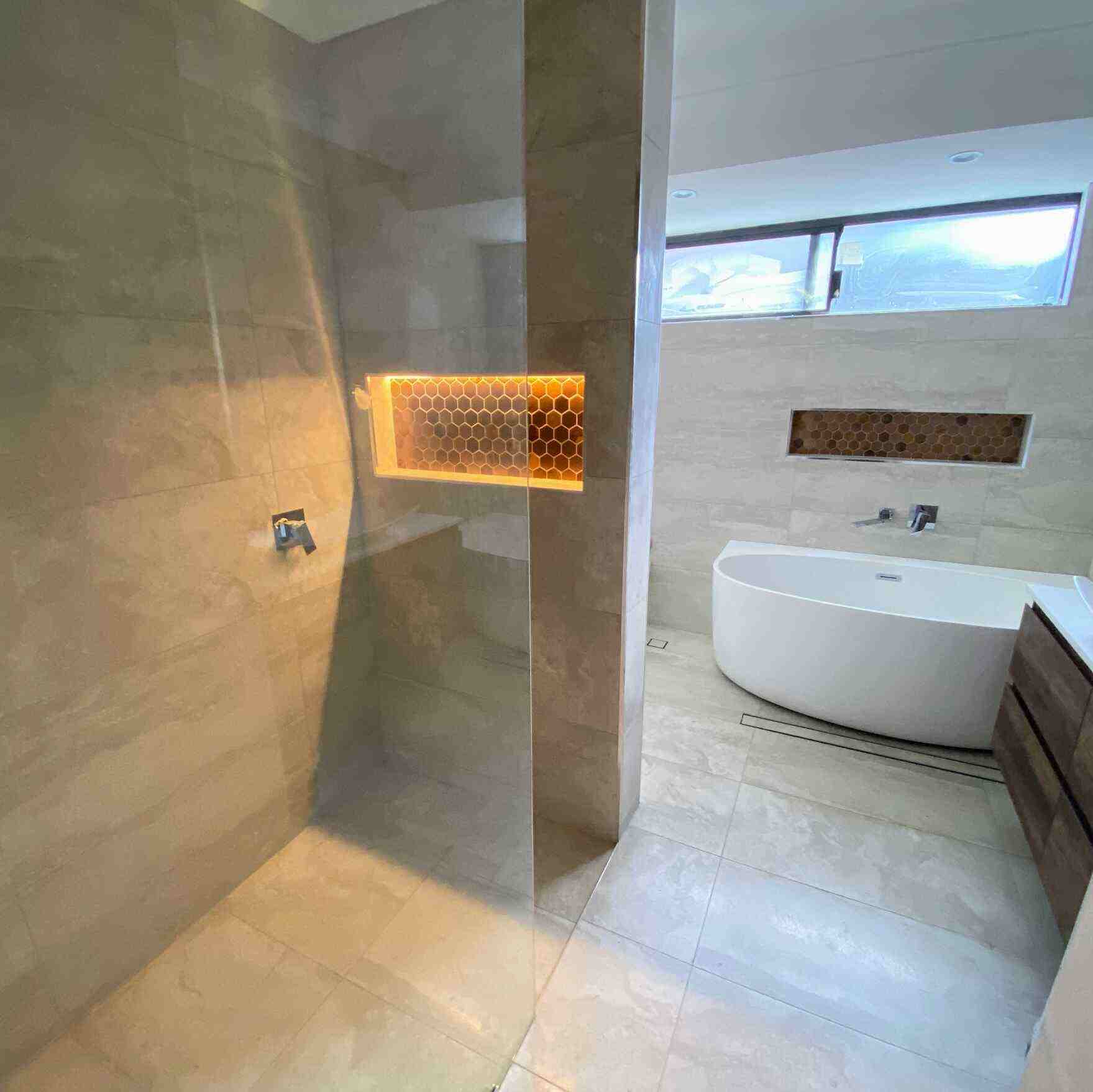 Luxury bathroom featuring a freestanding bathtub and a shower with a lit niche