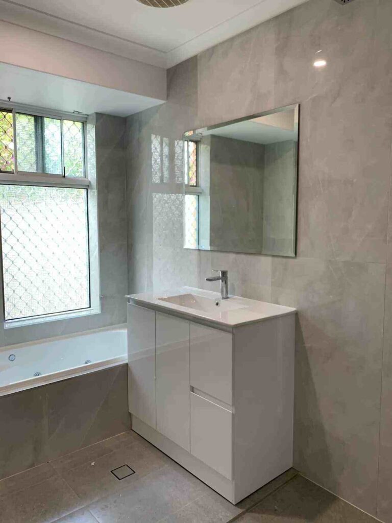 Modern bathroom with grey tiles and white vanity unit under a large mirror