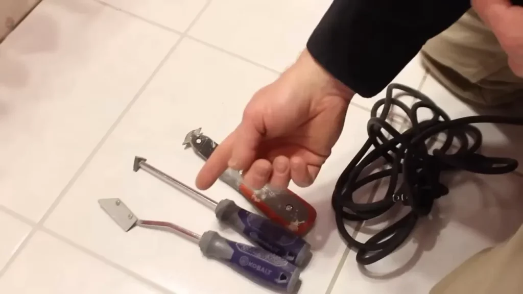 Reviewing tools like a scraper, screwdrivers, and extension cord for tile repair project.