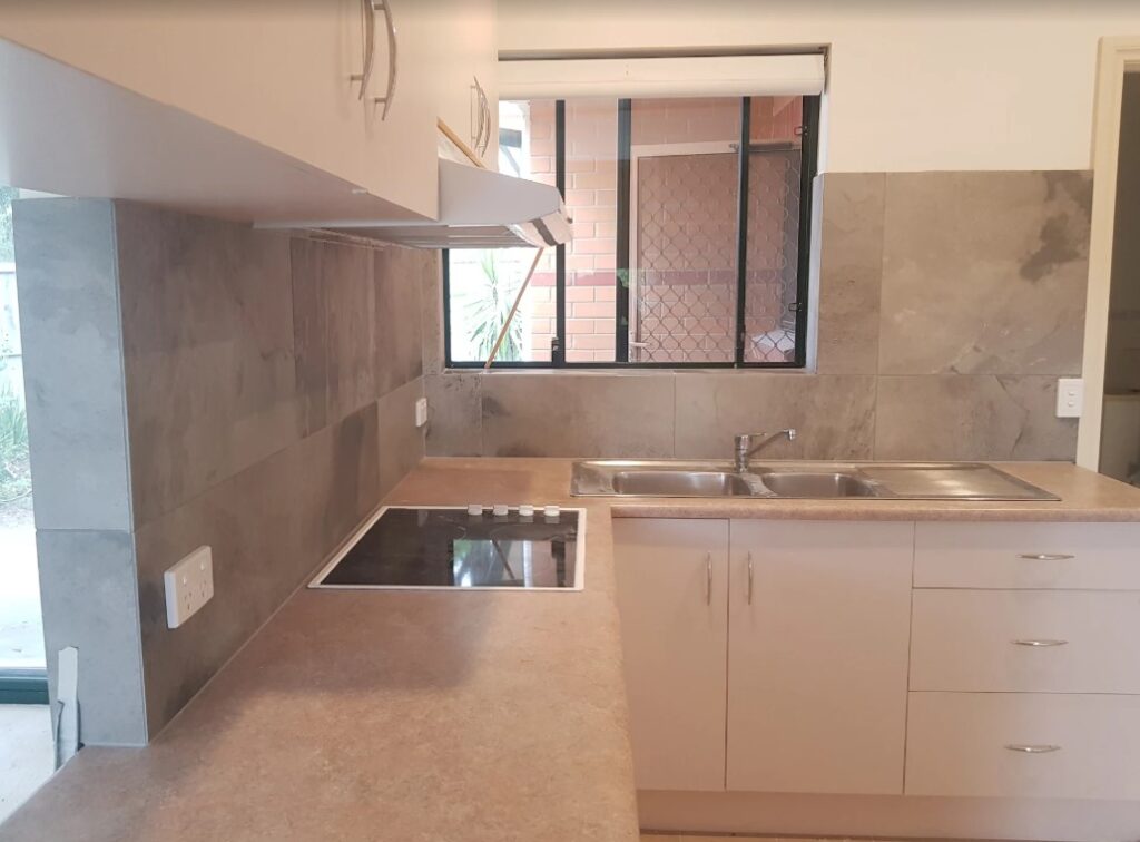 Neutral-toned kitchen with a stone-effect tile splashback and spacious countertops, installed by a Sydney kitchen tiler.